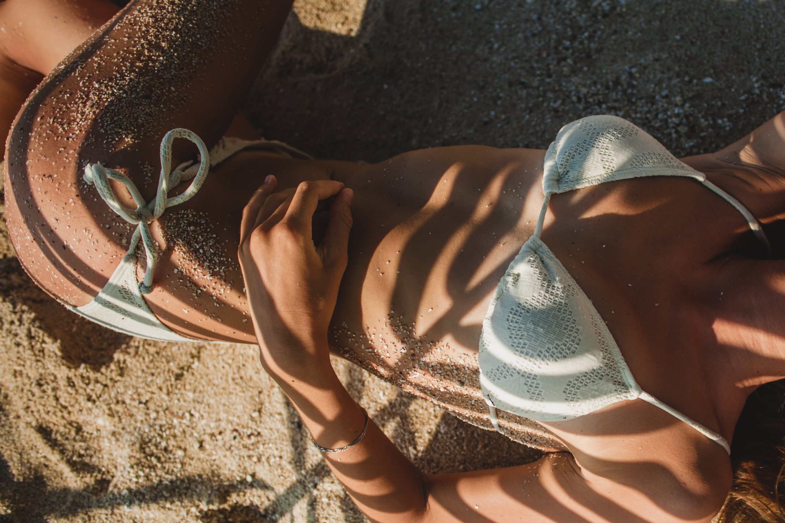 young-woman-laying-sand-beach-palm-tree-leaf-min